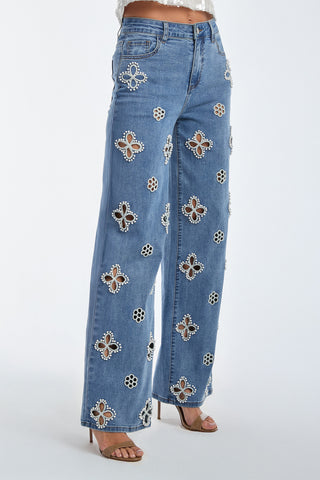 The Kaia Pearl High Rise Jean in medium blue features wide legs and unique oval and circular cut-outs, embellished with silver and white embroidered beaded flowers. They pair perfectly with open-toe sandals for a chic look.