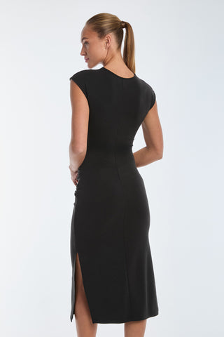 A person with a ponytail is seen from the back wearing the fitted Daphne Dress in black, featuring cap sleeves and a side slit. The subtle side ruching adds an elegant touch against the plain white background.