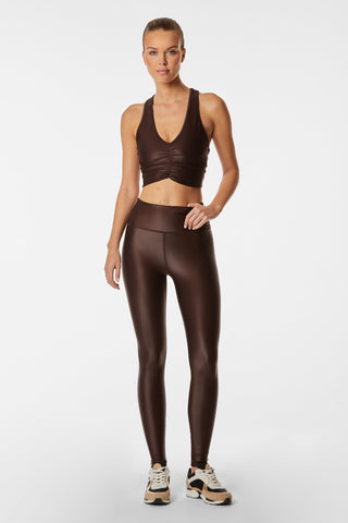 A woman wearing the Liquid Limitless Bra in Espresso and matching high-waisted leggings from her workout wardrobe stands against a plain white background. She is also wearing black, tan, and white sneakers. Her hair is pulled back into a sleek ponytail.