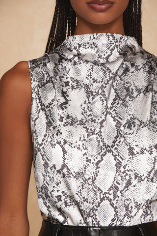 Close-up of a person wearing the Mara Top - Serpent, featuring a black and white snakeskin pattern. The elegant look is completed by the sleeveless mock neck design, while the person's braided hair is partially visible against a beige background.