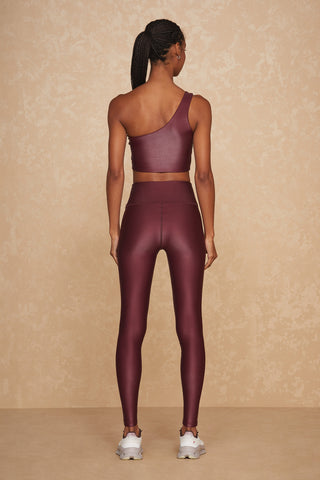 A person with a ponytail is wearing a Cherry Liquid Curve Bra and matching high-waisted leggings, standing with their back facing the camera. They are also wearing white sneakers. The background features a beige, textured wall.