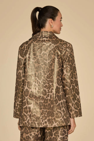 A person with long dark hair in a ponytail is wearing the Milan Gold Dusted Cargo Jacket - Leopard, featuring utility-inspired pockets and a metallic sheen, shown from the back against a plain beige background.