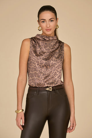 A person stands confidently, wearing the Mara Silk Top in a leopard print, paired with dark brown leather pants. They accessorize with gold hoop earrings and a gold bracelet against a soft beige backdrop.