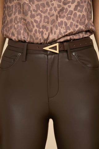 A close-up of a person wearing dark brown faux leather pants with the chic Amelia Belt - Espresso, featuring a triangular buckle. The top is sleeveless and boasts a leopard-print pattern, creating a stylish and modern look.