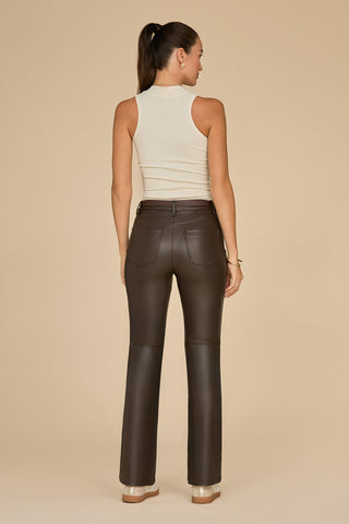 With her long dark hair in a ponytail, a woman stands with her back to the camera, showcasing the Kai Leather Pant in Espresso. She pairs these chic high-rise trousers with a sleeveless beige top and matching platform heels, all set against a plain beige background.