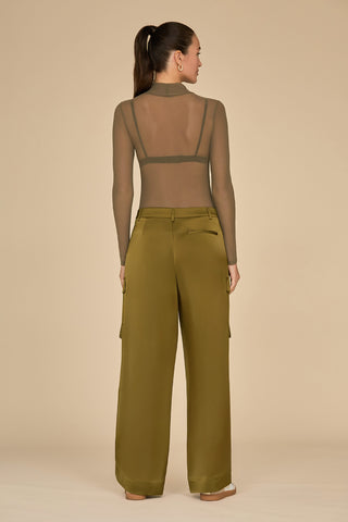 A person stands with their back to the camera, wearing a sheer long-sleeve top paired with the Milan Satin Cargo Pant in olive. The background is plain beige.