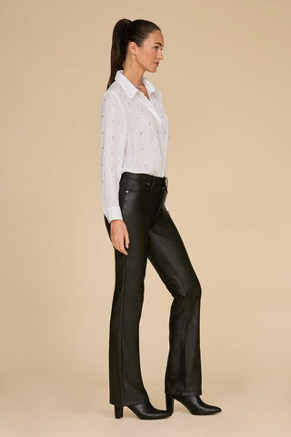 A woman in profile stands against a neutral background, dressed in the Aniya Crystal Shirt - White and black leather pants. She complements the look with black heeled boots and styles her hair in a ponytail.