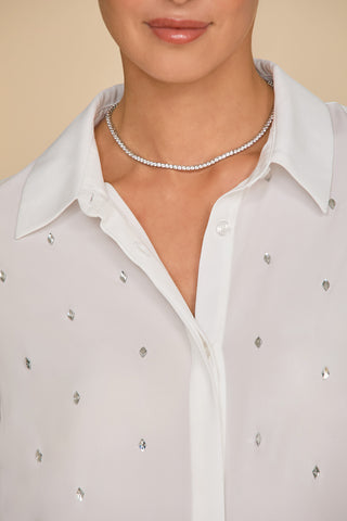 Wearing the Aniya Crystal Shirt in white, featuring subtle diamond-patterned crystal embellishments, this person pairs it elegantly with a simple silver necklace against a soft beige backdrop.