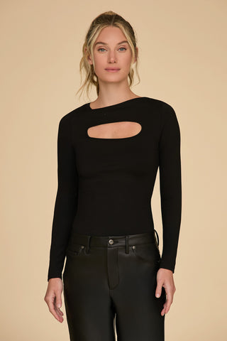 A person with blonde hair is wearing the Jada Cut Out Long Sleeve Top in black, paired with matching black pants. They pose against a simple beige backdrop, gazing at the camera with a neutral expression.