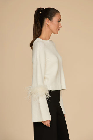 Side profile of a person with long hair in a ponytail, wearing the "Bella Feather Trim Sweater - Pearl" and black pants, standing against a beige background.