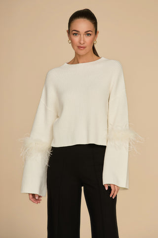 A person with long hair is wearing a Bella Feather Trim Sweater in Pearl and black pants, standing against a beige background.