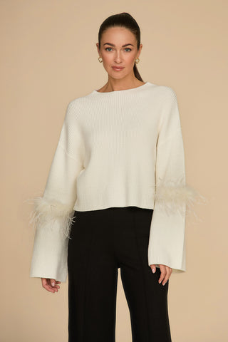 The person with long hair wears the luxurious Bella Feather Trim Sweater in pearl, featuring feather-trimmed sleeves, and black pants, set against a beige background.