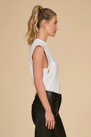 A woman with wavy blonde hair in a ponytail is shown in profile against a beige background. She is wearing a sleeveless white Dylan Crystal Top paired with black trousers, seamlessly blending style and elegance into her ensemble.