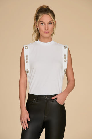 A person with long hair is wearing a Dylan Crystal Top - White, a sleeveless muscle tank with embellished shoulders, paired with black leather pants. They are standing against a beige background, looking at the camera with a neutral expression.