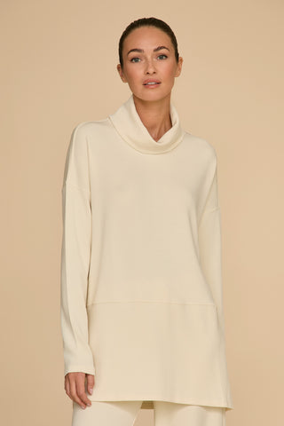 A person with their hair tied back is wearing the Pearl long-sleeved Daphne Top, crafted from a soft modal blend and featuring a cowl neck, perfect for the ultimate on-the-go look. The background is a neutral beige.