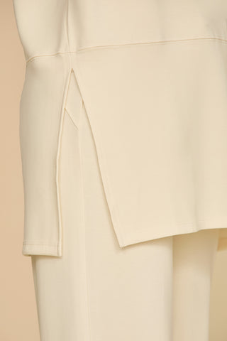 Close-up of a beige layered garment showcasing the Daphne Top - Pearl with a slit side detail over coordinating pants. Made from a soft modal blend, it provides the perfect on-the-go look, achieving a minimalist and elegant appearance against a light background.