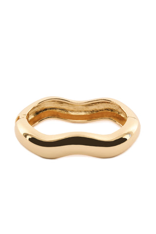 The Paloma Bangle - Gold showcases a wavy design with a smooth, shiny surface and an abstract, organic shape. This elegant piece of jewelry features a wide band and an irregular outline, embodying a modern, artistic appearance.