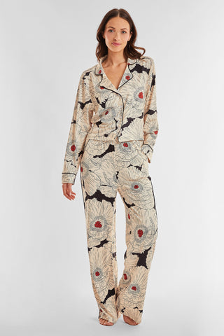 A person wearing the Poppy Pajama Soft Long Pant set with a floral poppy print. The pajama top features long sleeves and a collar, while the high-waist cut pants are full-length. The fabric showcases large cream-colored flowers with red centers and black leaves, all set against a light background.