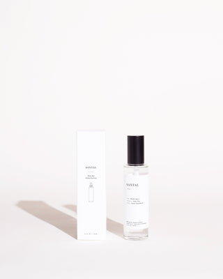 Minimalist-style product image featuring a bottle of Santal Room Mist by Brooklyn Candle Studio next to its white rectangular box. The 100% vegan bottle is clear with a black cap and simple labeling. Infused with essential oils like Hinoki Cypress, the sleek packaging offers ample white space and clean typography.